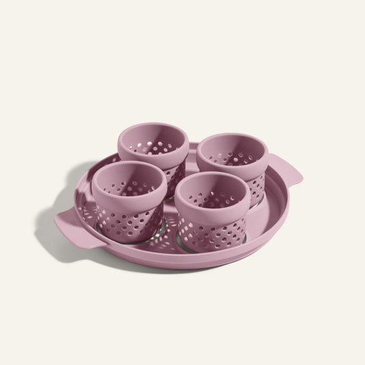 The Egg Poacher includes four pink silicone cups for poaching eggs, all arranged on a matching round plastic tray with handles.