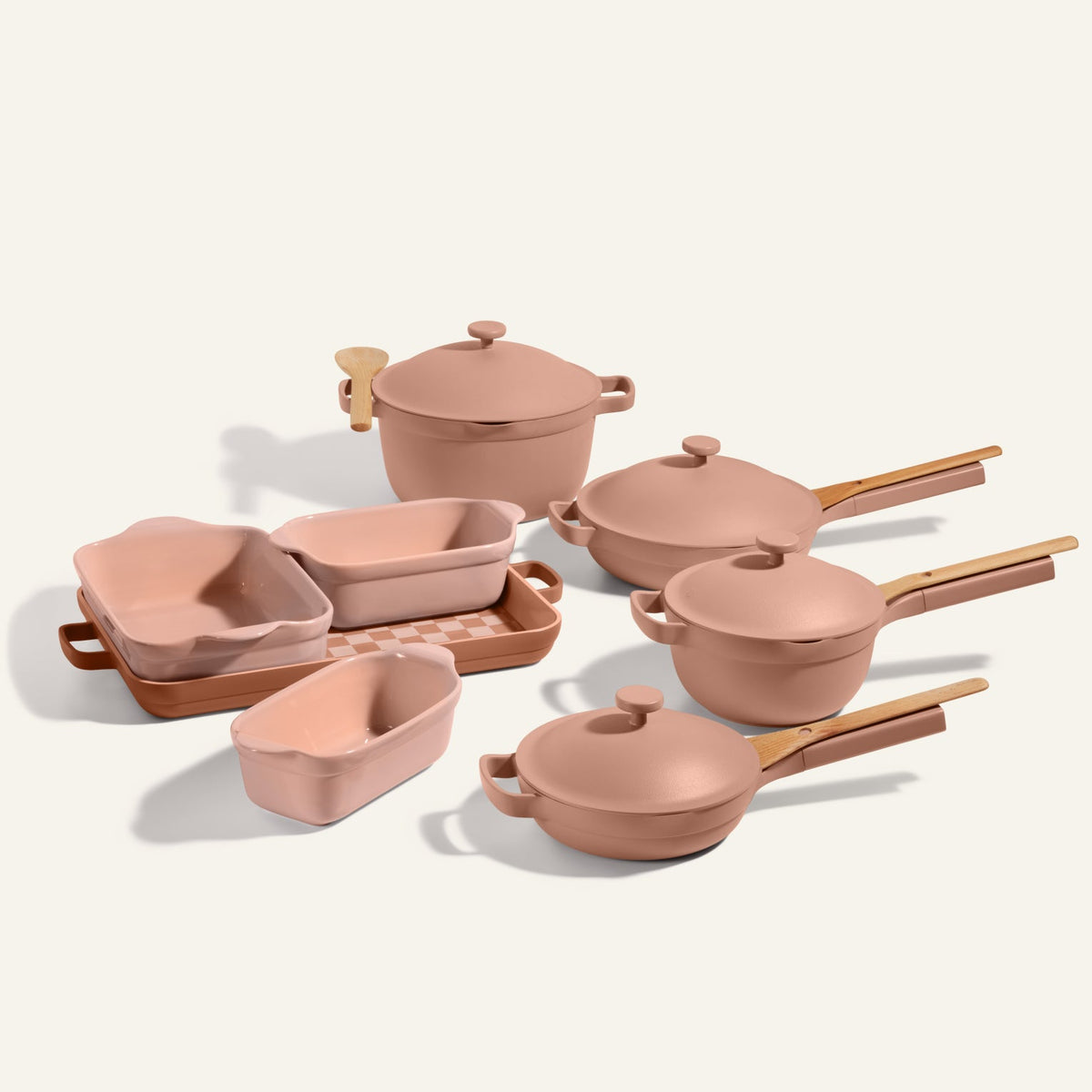 A pink Cookware + Bakeware Set with ceramic pots, saucepans, bakers, loaf pans, and wooden accents is arranged on a light background—perfect for fans of stylish cookware like the Always Pan or Perfect Pot.