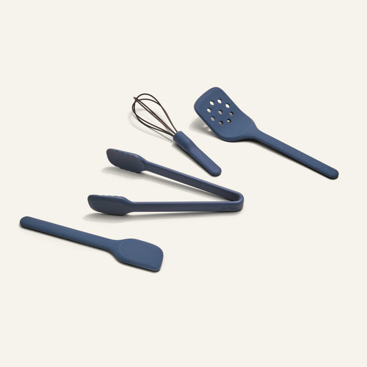 Four blue Mini Utensil Essentials—spatula, tongs, whisk, and slotted turner—are arranged on a plain light background.
