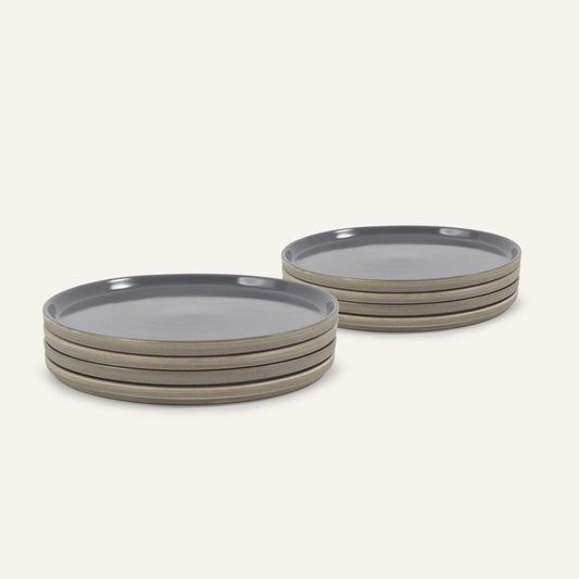Two stacks of Main Plates, round and hand-painted gray with beige sides, are arranged on a light background. Each stack has four plates, highlighting a modern minimalist style that’s both functional and stylish.