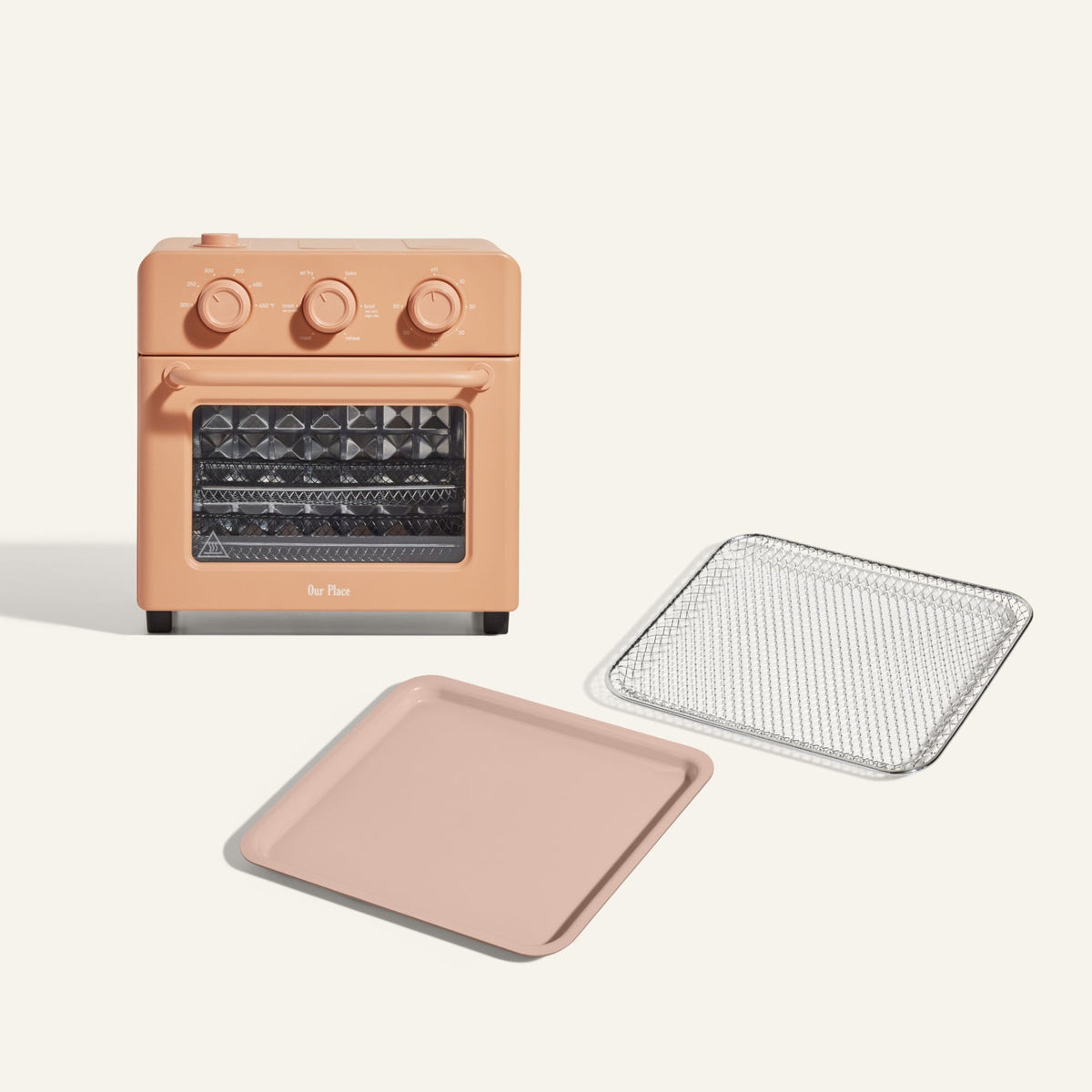 The Wonder Oven + Wonder Oven Essentials Kit in peach is displayed with three dials, a matching baking tray, and a metal mesh tray on a light background.