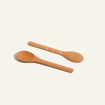 Two Beechwood Spoons are placed side by side on a plain background. Made from beechwood, one handle features a groove for grip while the other is smooth, combining style and practicality in your kitchen utensils.