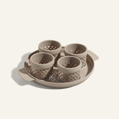 The Egg Poacher includes a beige tray and four matching perforated silicone cups, ideal for poaching eggs, all crafted from the same material and displayed against a light background.