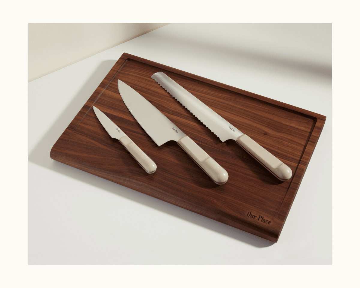 A wooden cutting board with three beige-handled kitchen knives, including the Everyday Chef’s Knife with a full-tang German steel blade, plus a paring knife and a serrated bread knife.