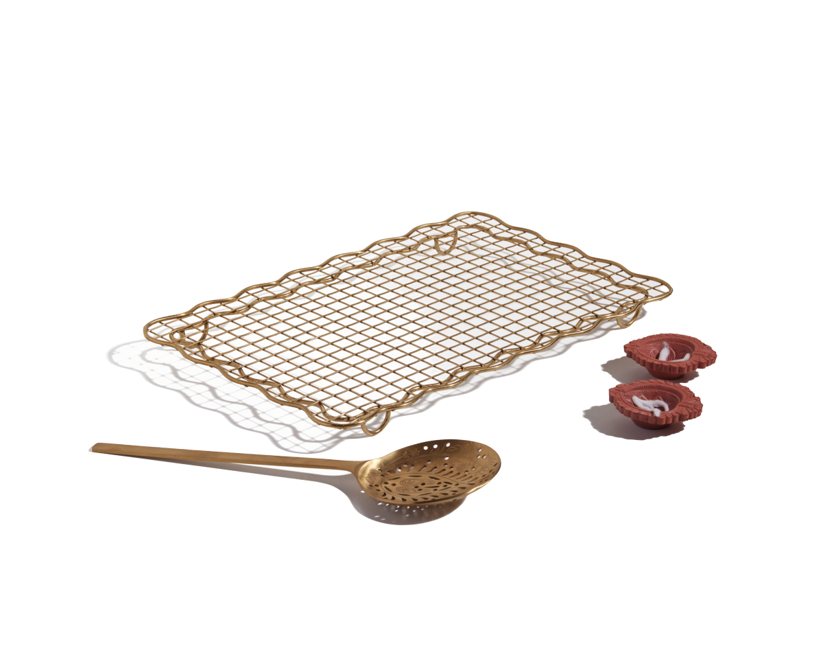 The Golden Fry Set—featuring a rectangular gold cooling rack and skimmer spoon—is arranged with three pink rolled pastries on a white background, making it perfect for an elegant Diwali celebration.