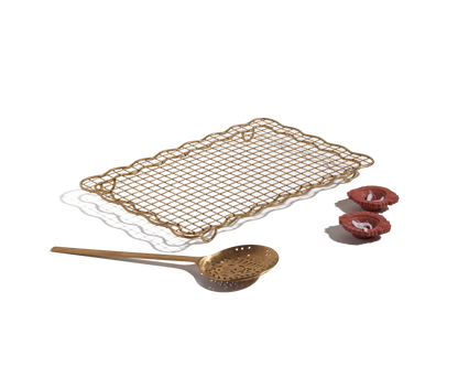 The Golden Fry Set—featuring a rectangular gold cooling rack and skimmer spoon—is arranged with three pink rolled pastries on a white background, making it perfect for an elegant Diwali celebration.