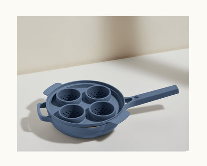A blue Egg Poacher with four built-in silicone cups for perfectly poached eggs sits on a white surface against a neutral background.
