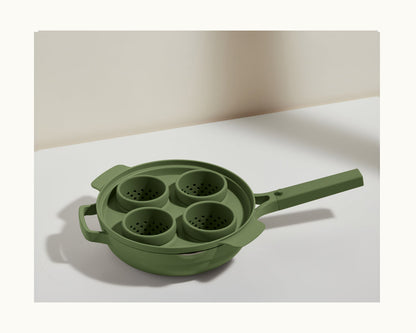 The Egg Poacher features a green multi-section design with four perforated silicone cups, a main handle, and an extra side handle—ideal for poaching eggs—shown on a white surface.