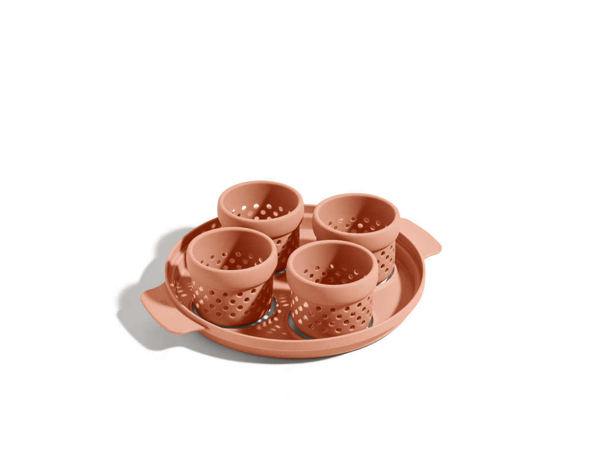 The Egg Poacher features four terra-cotta-colored silicone cups with holes in a matching round tray, ideal for making poached eggs, displayed on a plain white background.