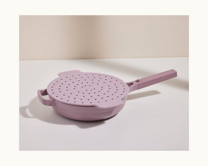 A lavender-colored Fearless Fry pan with a matching perforated lid and long handle sits on a white surface, easily preventing splatters against a neutral background.