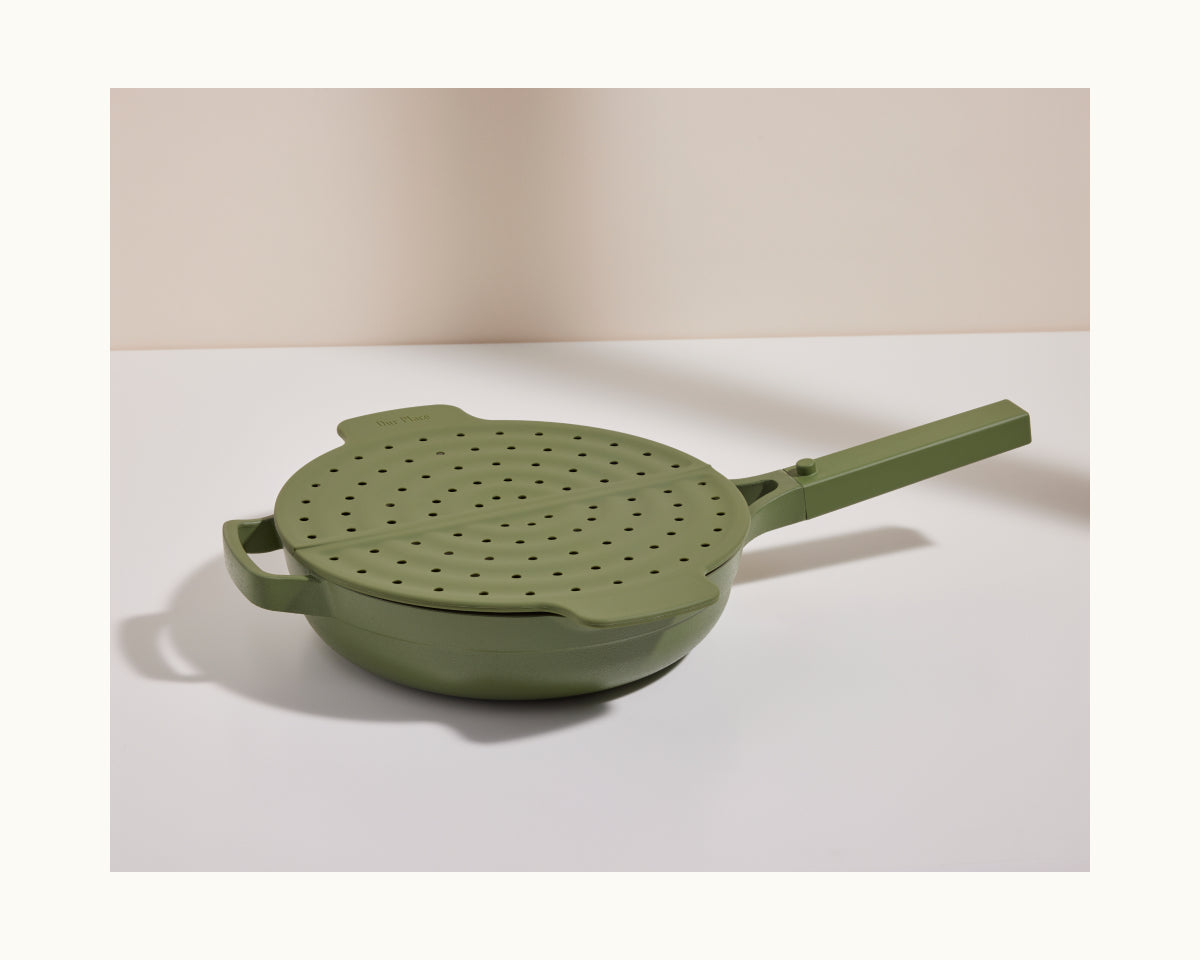 The Fearless Fry cooking pan in green features a long handle and comes with a matching perforated lid for splatter prevention, shown on a white surface with a neutral background.