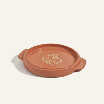 The Flipping Platter is a round, shallow terracotta baking dish with side handles and a floral pattern on the base, ideal for serving maqluba or tahdig.