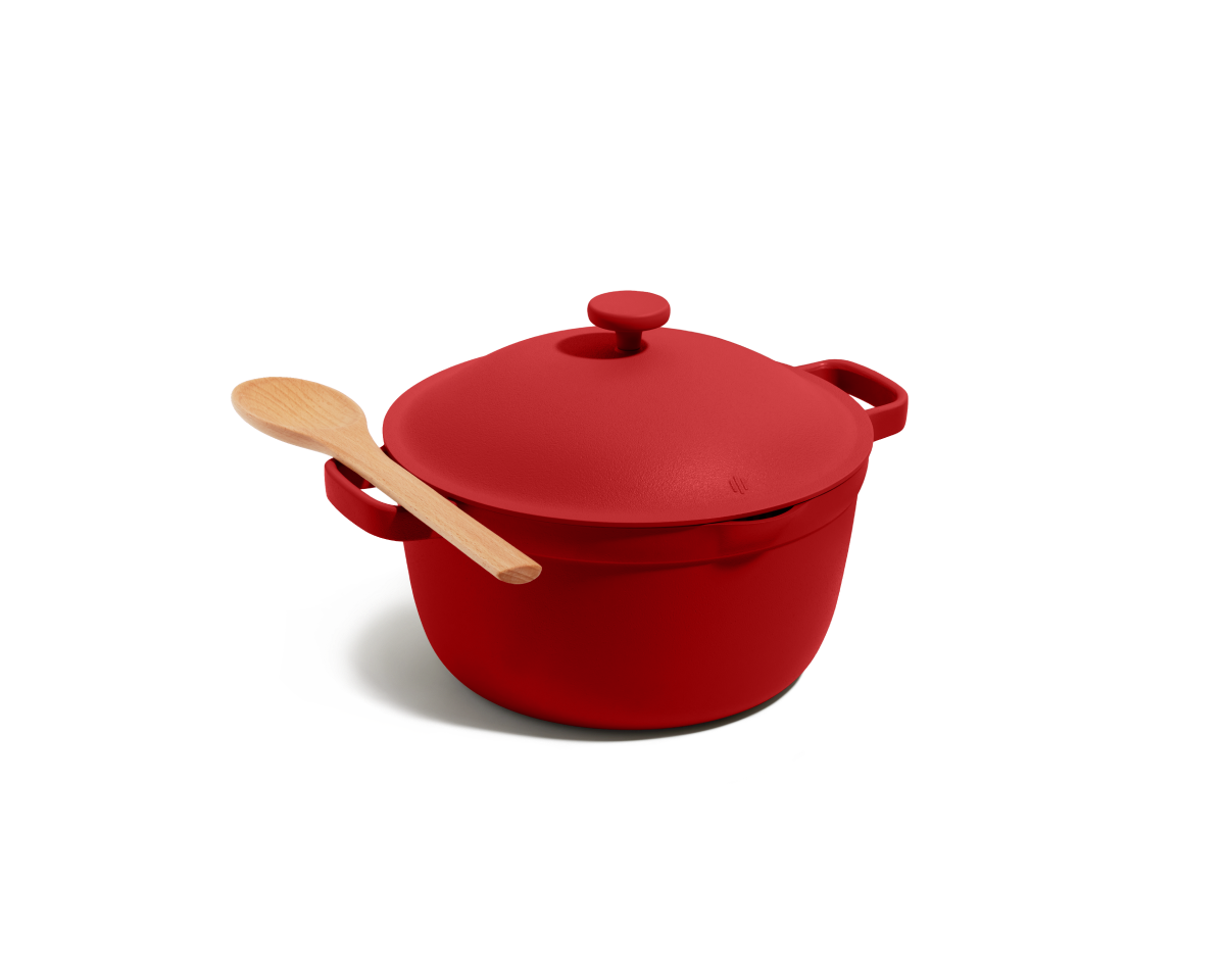 The Perfect Pot, a red family-sized Dutch oven with a matching lid and a wooden spoon on top, set against a plain white background.