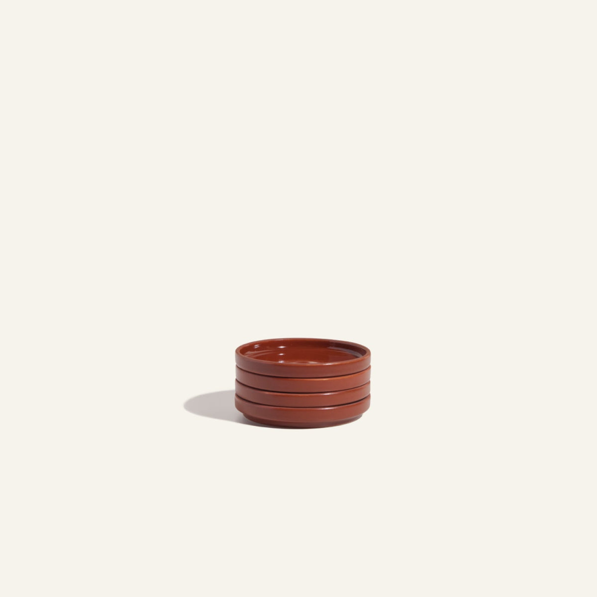 A stack of three round, shallow ceramic Tiny Plates in a reddish-brown hue rests on a plain background—an elegant addition to any table setting.