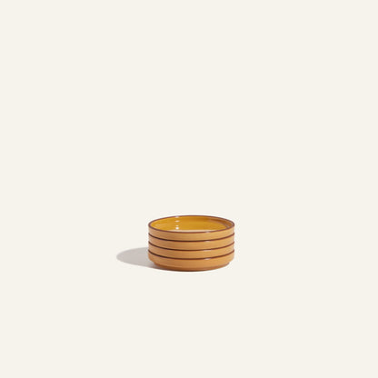 A stack of three Tiny Plates—round, yellow ceramic snack plates with dark brown rims—sits on a plain light background.