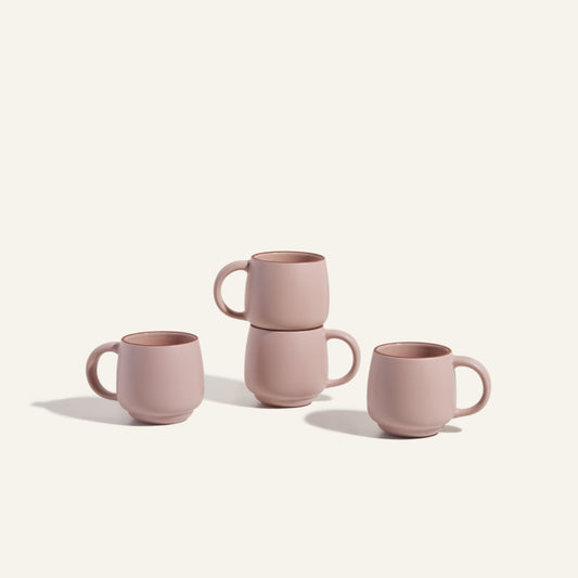 Four Night + Day Mugs in matte pink ceramic stoneware, each with a generous capacity, are arranged on a light background—two stackable ones in the center and two placed on either side.
