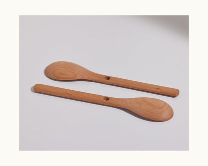 Two Beechwood Spoons with holes in the handles are placed parallel on a plain white surface, highlighting these elegant kitchen utensils for everyday use.