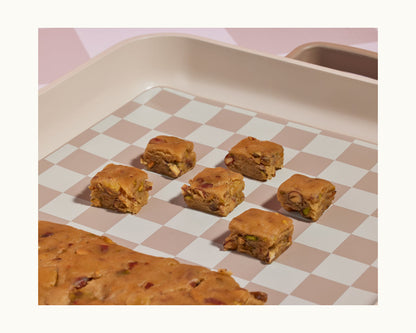 A baking tray from the Bakeware Set features a checkered pattern, holding six evenly spaced dough cubes and a larger piece in the corner.