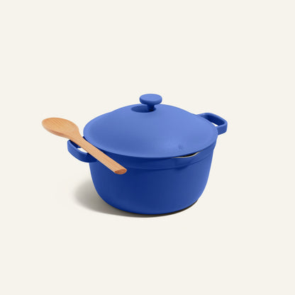 The Perfect Pot, an 8-in-1 blue nonstick pot with a lid, features a wooden spoon resting on its handle and is displayed against a plain light background.
