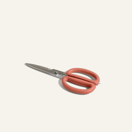 The Shear Genius kitchen shears feature stainless steel blades, built-in herb strippers, and large coral handles, shown on a light, neutral background.