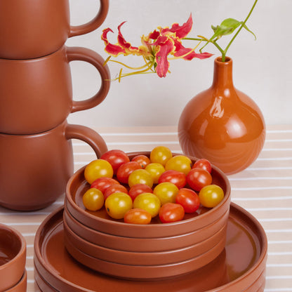Stacked terracotta mugs and dessert plates with tomatoes