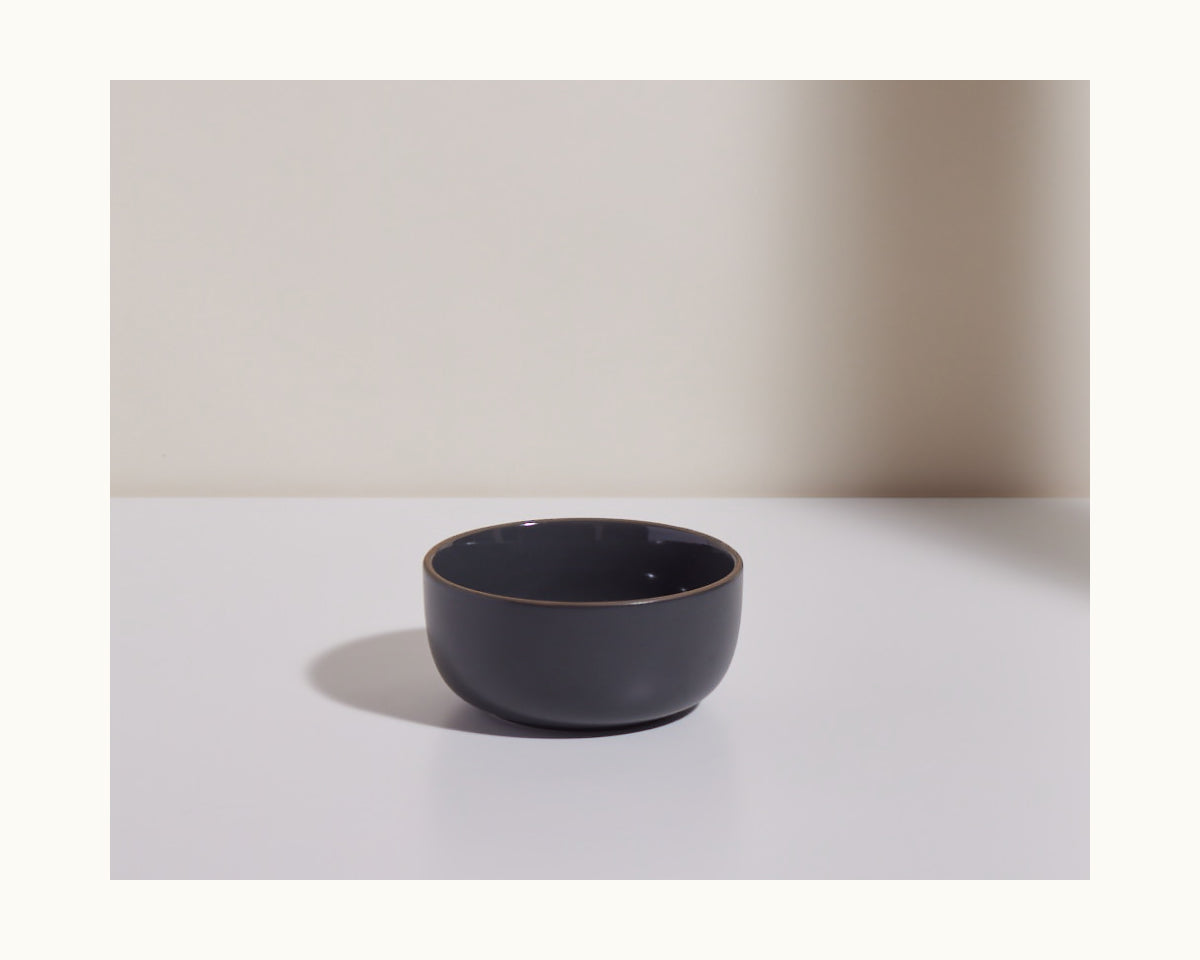 A dark gray Soup Bowl from a stackable set rests on a white surface against a light background, casting a soft shadow to the left.