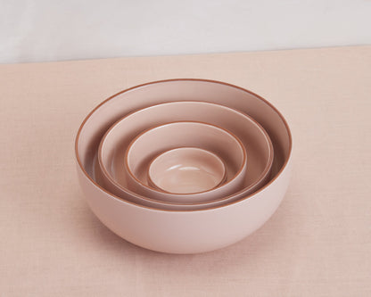 Four light pink Tiny Bowls of different sizes are stacked together on a matching surface, highlighting elegant, scratch-resistant, and stackable ceramic tableware.