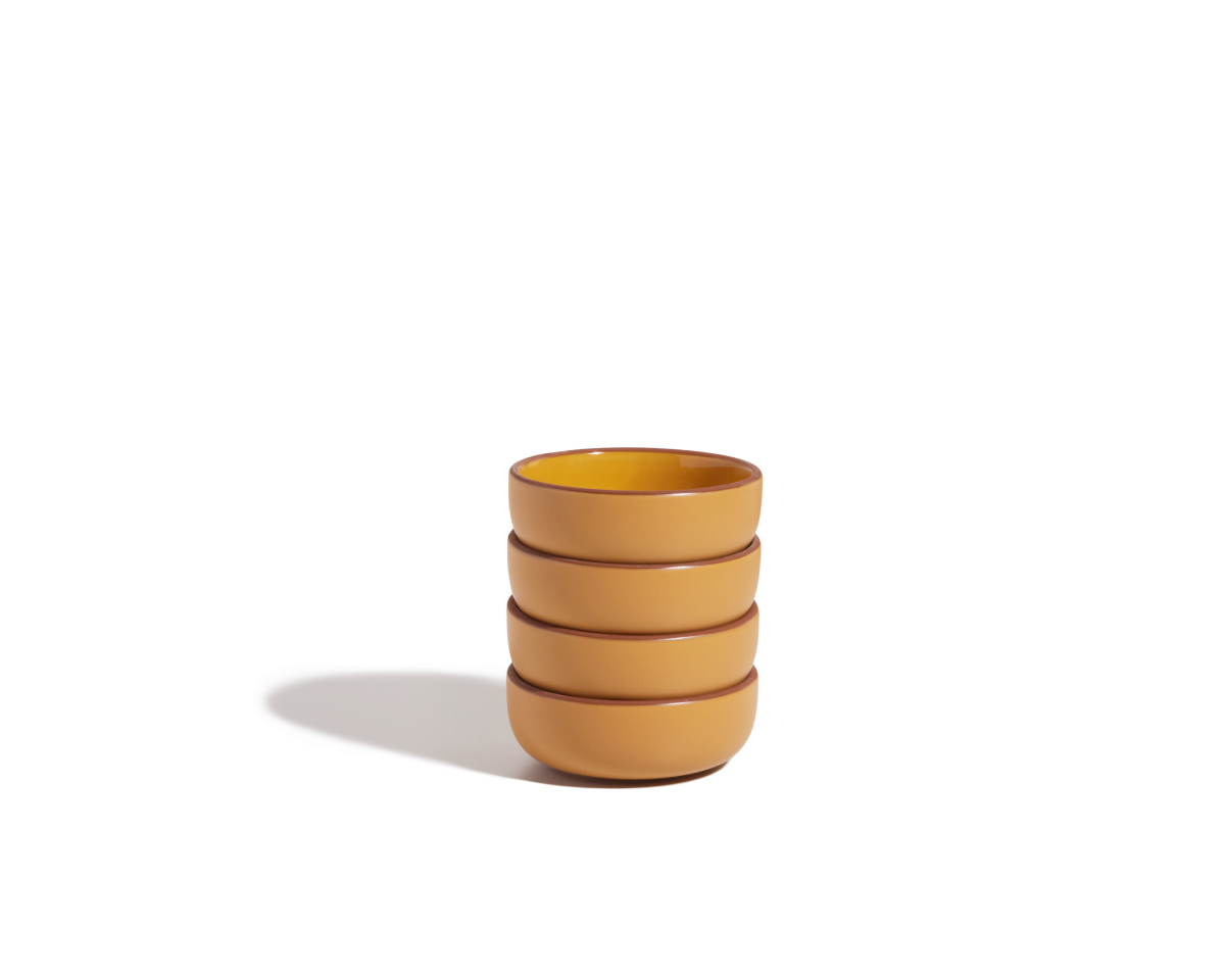 A stack of four yellow, scratch-resistant Tiny Bowls sits on a plain white background, casting a soft shadow to the left—these bowls are perfect stackable tableware for everyday use.