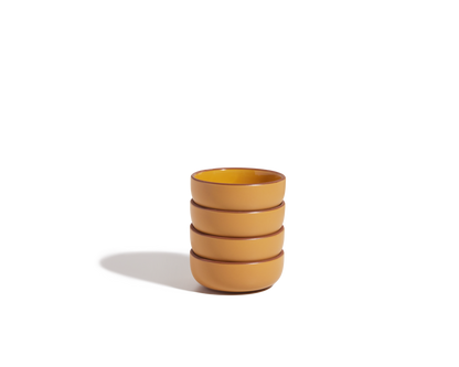 A stack of four yellow, scratch-resistant Tiny Bowls sits on a plain white background, casting a soft shadow to the left—these bowls are perfect stackable tableware for everyday use.