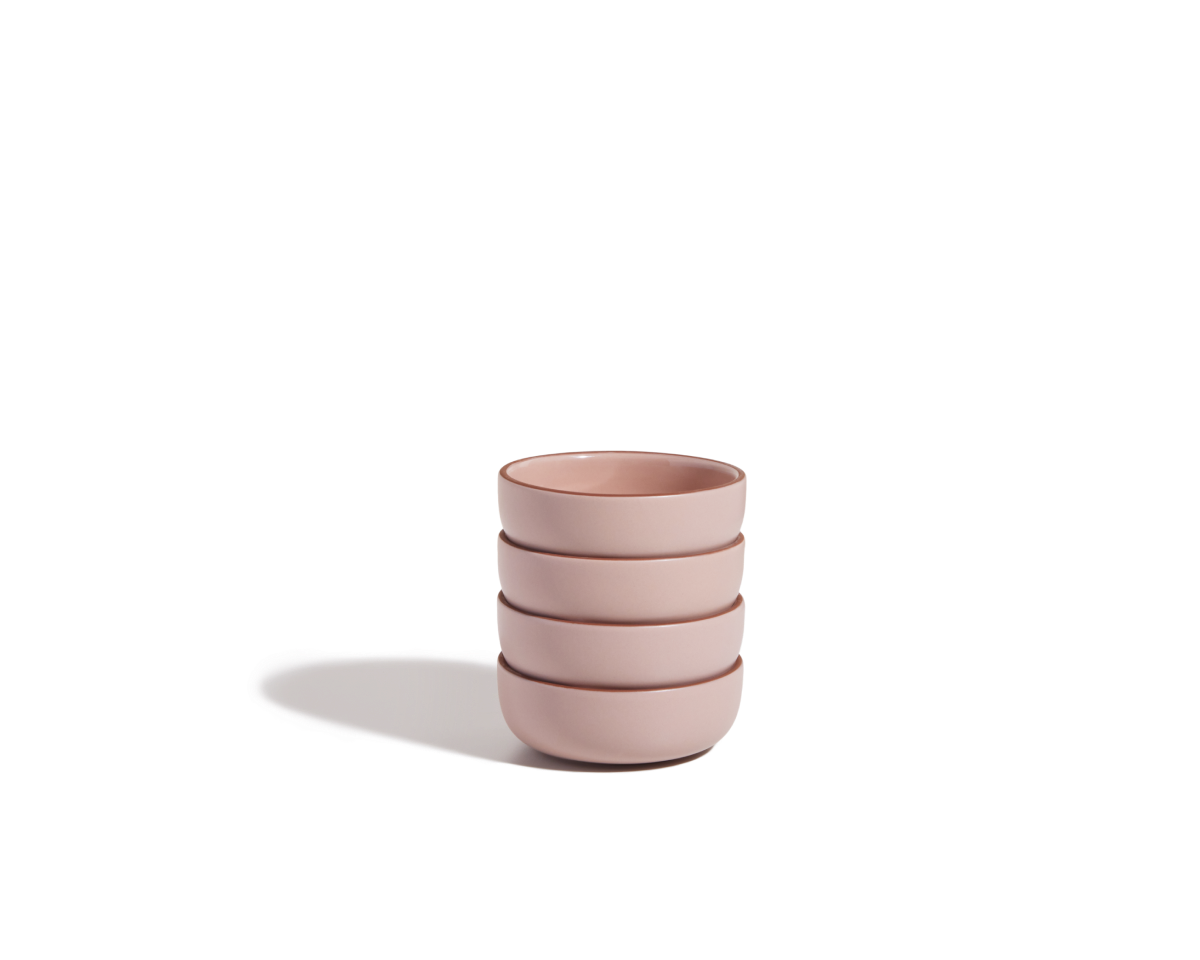 A stack of four pink Tiny Bowls, made from scratch-resistant ceramic, sits on a plain white surface with a shadow to the left, highlighting their elegant and stackable design.