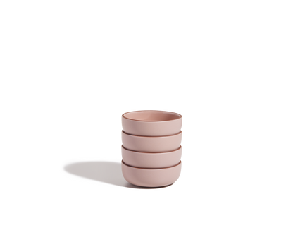 A stack of four pink Tiny Bowls, made from scratch-resistant ceramic, sits on a plain white surface with a shadow to the left, highlighting their elegant and stackable design.