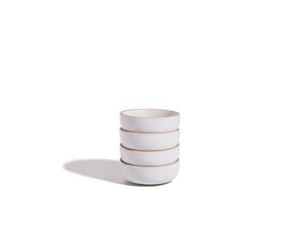 A stack of four Tiny Bowls, white ceramic with light brown rims and scratch-resistant surfaces, is shown on a plain white background with a shadow to the left.
