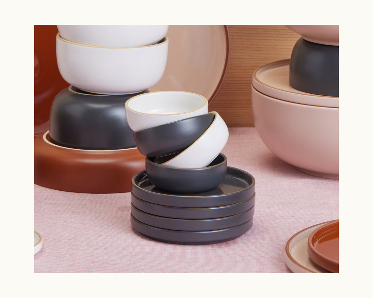 A neatly stacked set of scratch-resistant Tiny Bowls in white, gray, and terracotta rests on a pink tablecloth.