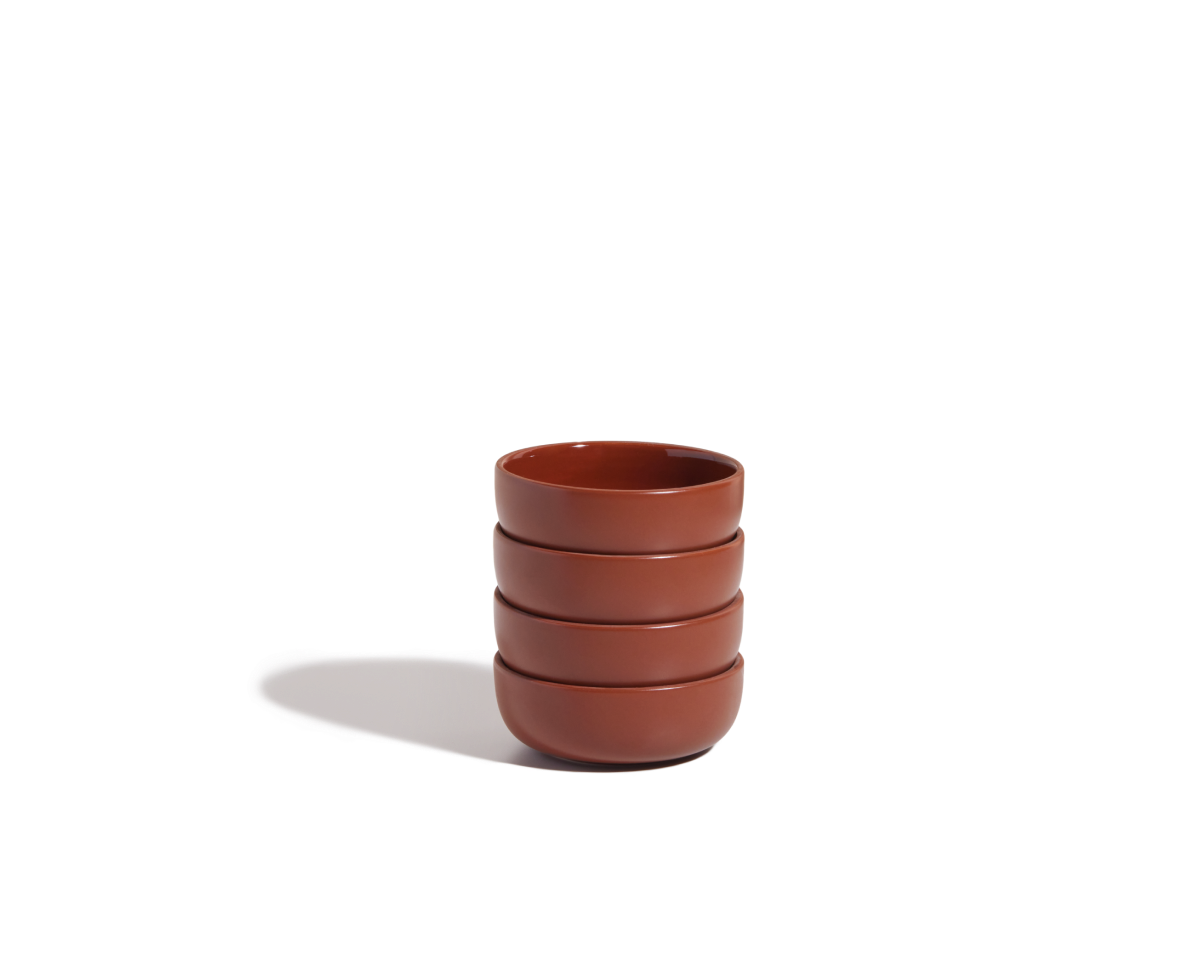 A stack of four Tiny Bowls—round, reddish-brown, ceramic, scratch-resistant, and stackable—rests on a white background with a soft shadow to the left.
