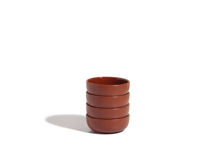 A stack of four Tiny Bowls—round, reddish-brown, ceramic, scratch-resistant, and stackable—rests on a white background with a soft shadow to the left.