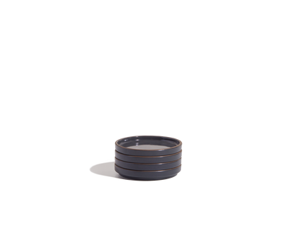 The Tiny Plates are small, round, dark gray ceramic plates with horizontal ridges along the sides, ideal as snack plates and showcased on a plain white background.