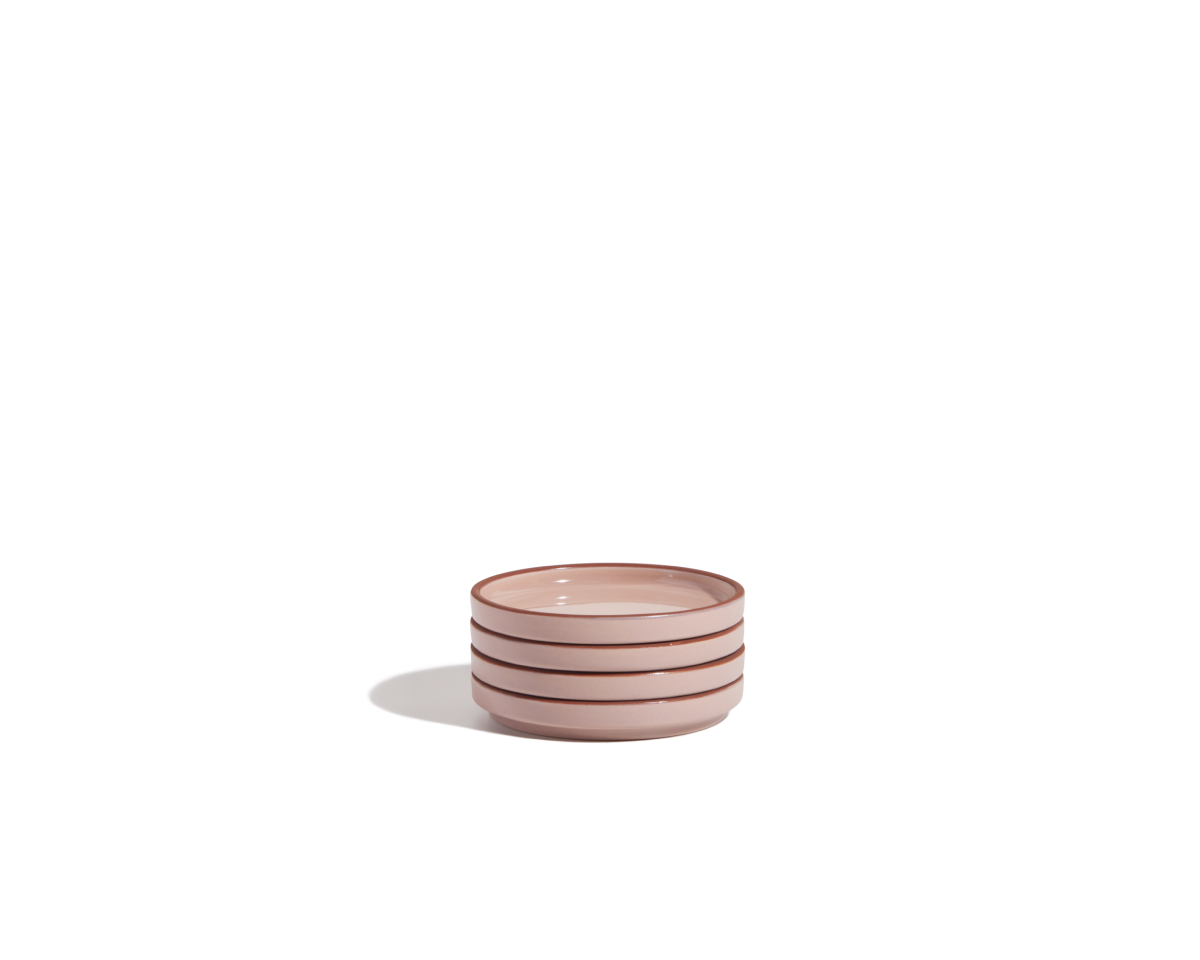 A small stack of three light pink Tiny Plates with brown rims, part of a stylish tableware set, placed against a plain white background.
