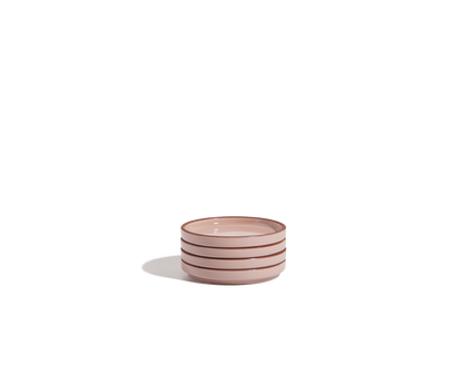 A small stack of three light pink Tiny Plates with brown rims, part of a stylish tableware set, placed against a plain white background.