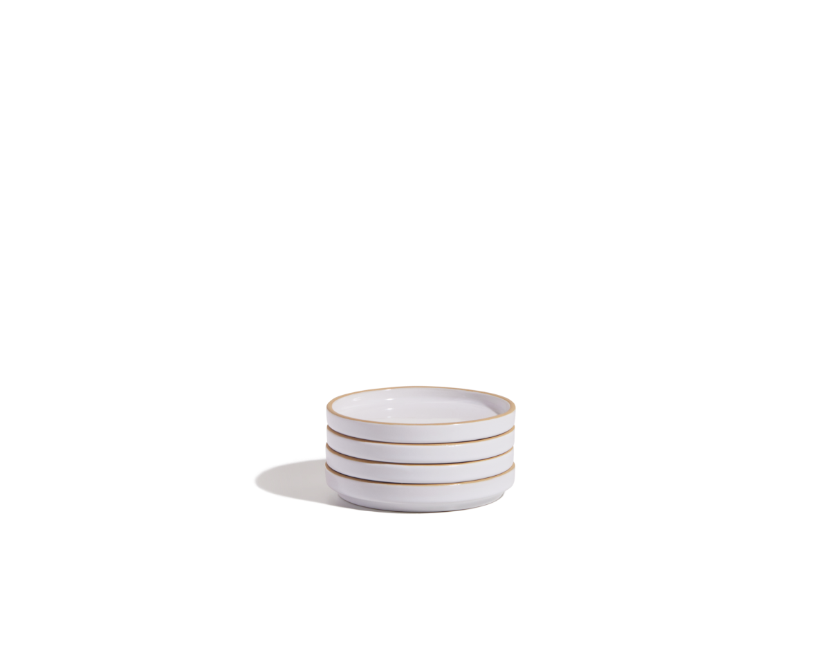 A stack of three small, white ceramic Tiny Plates with thin gold rims, part of an elegant tableware set, placed on a plain white background.