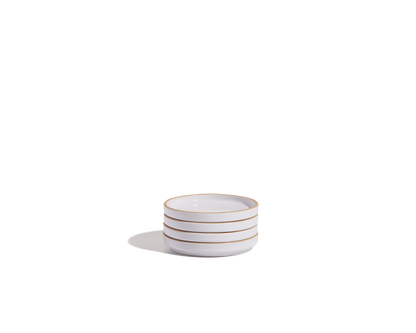 A stack of three small, white ceramic Tiny Plates with thin gold rims, part of an elegant tableware set, placed on a plain white background.