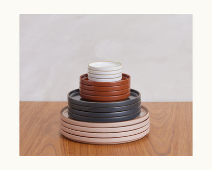 Tiny Plates, a set of round ceramic dishes and bowls in assorted sizes and colors, are stacked neatly on a wooden surface against a light background—perfect for creating a charming snack plate presentation.