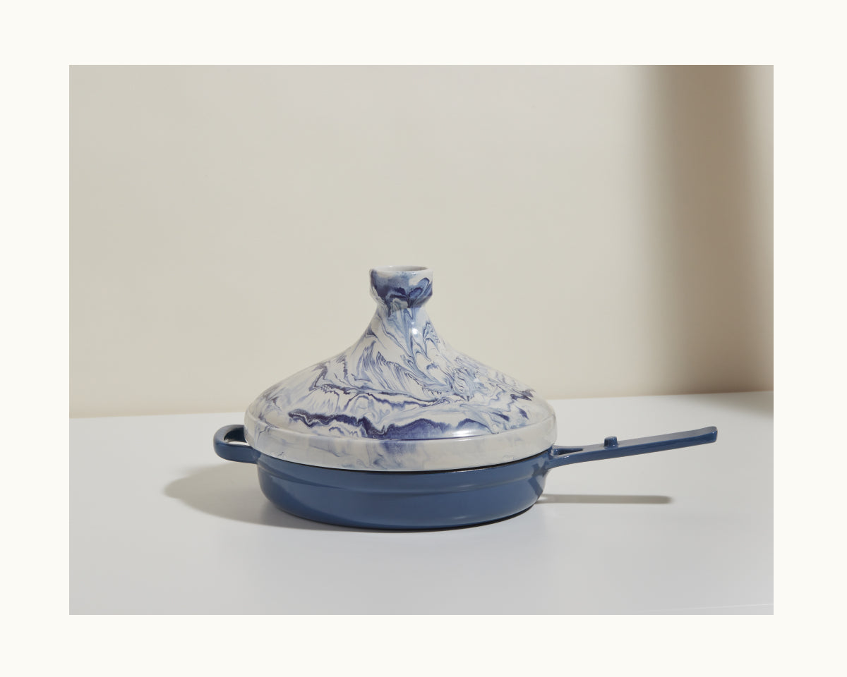 A handcrafted blue and white marbled Tagine pot with a handle rests on a white surface against a neutral background, highlighting Moroccan artistry—ideal for slow cooking flavorful dishes.