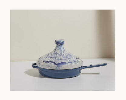 A handcrafted blue and white marbled Tagine pot with a handle rests on a white surface against a neutral background, highlighting Moroccan artistry—ideal for slow cooking flavorful dishes.