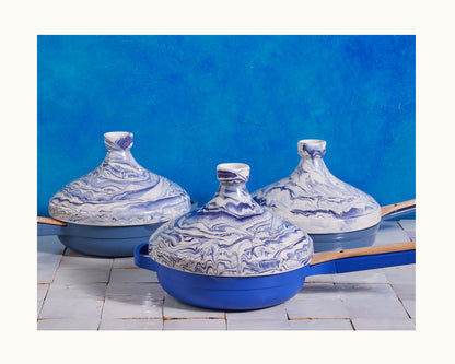 Three blue and white marbled clay Tagine pots with wooden handles are displayed on a tiled surface against a bright blue background, highlighting Moroccan craftsmanship and perfect for slow-cooking.