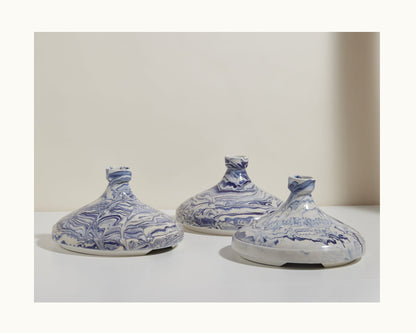 Three Tagine ceramic vessels with wide, rounded bases and narrow necks feature blue and white marbled patterns. Displayed on a white surface, they evoke the look of traditional tagines against a neutral backdrop.