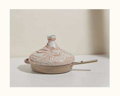 The Tagine is a handcrafted Moroccan clay pot with a swirled beige and brown lid and a long handle, perfect for slow-cooking flavorful dishes.