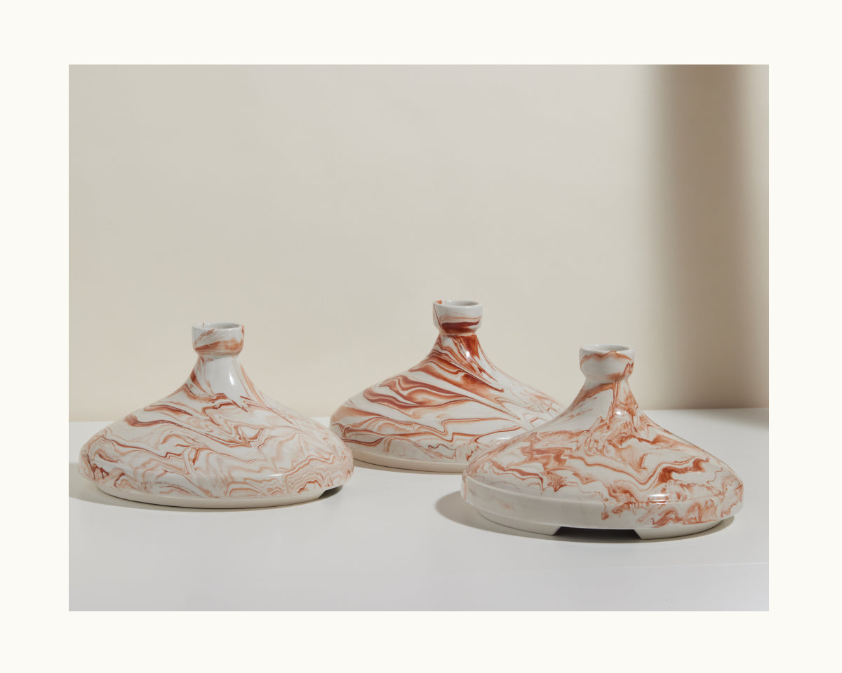 Three handcrafted Tagine vessels, featuring wide bases and marbled red-and-white patterns, are displayed on a white surface against a neutral backdrop.