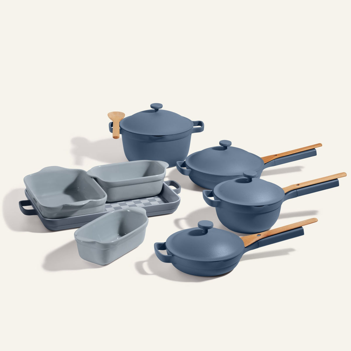 A blue Cookware + Bakeware Set with pots, pans, baking dishes, lids, and light wooden handles is displayed on a neutral background—perfect to pair with your favorite Perfect Pot or Always Pan.