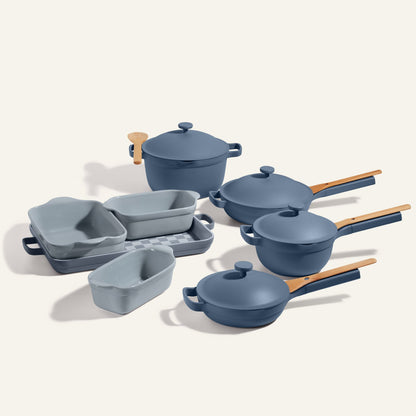 A blue Cookware + Bakeware Set with pots, pans, baking dishes, lids, and light wooden handles is displayed on a neutral background—perfect to pair with your favorite Perfect Pot or Always Pan.