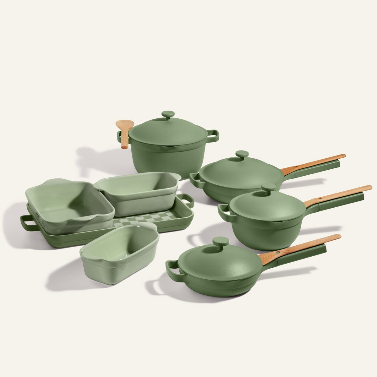 A green Cookware + Bakeware Set with wooden handles, featuring items like pots, pans, and baking dishes including the Perfect Pot and Always Pan, is arranged on a light background.